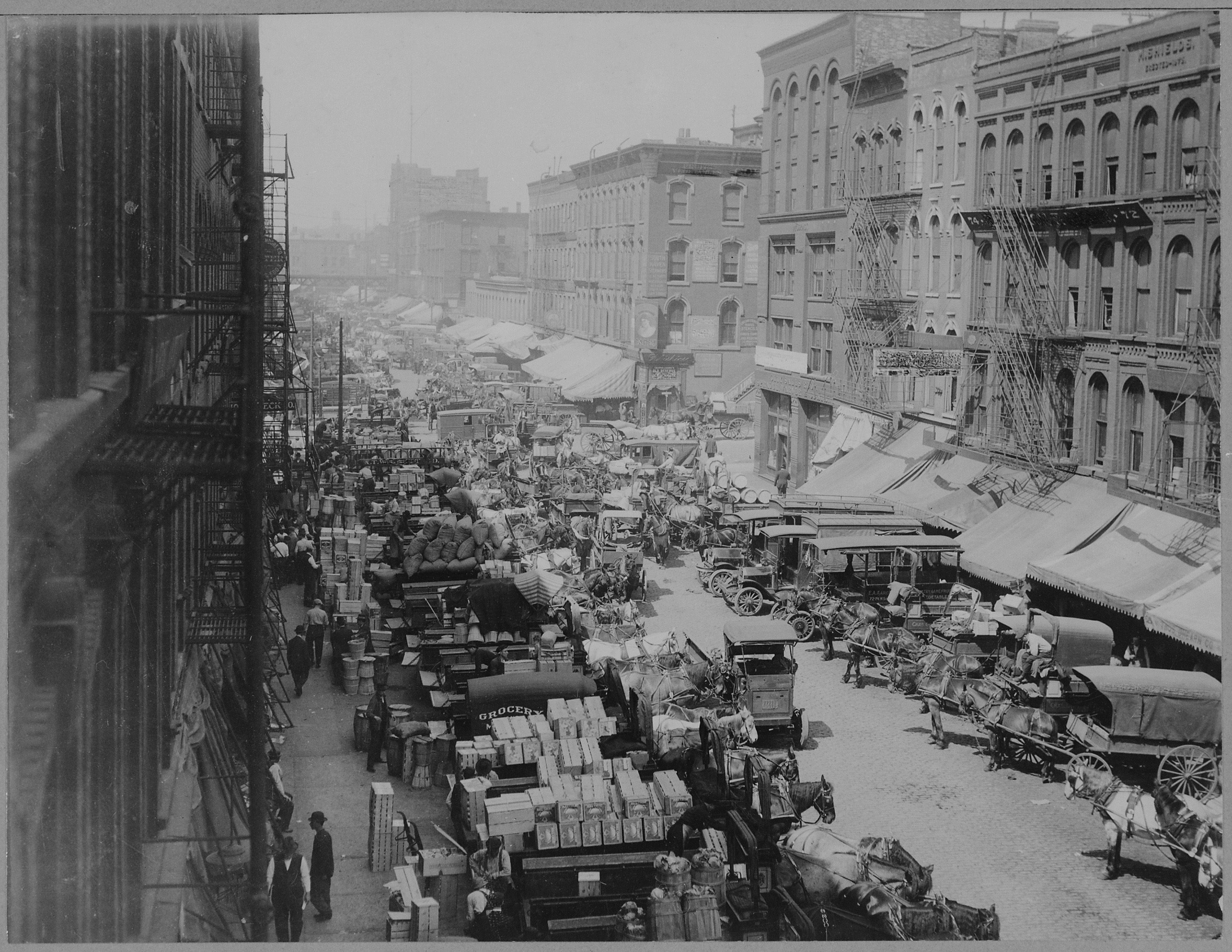 A crowded market street with horse carts and grocery stalls, early twentieth century